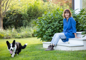 Abbey sitting on white stairs in front of house while her dogs runs happily in the green grass.